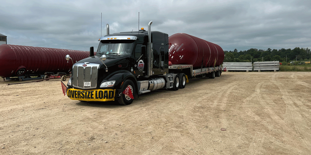 Black semi-truck hauling large red tanks.