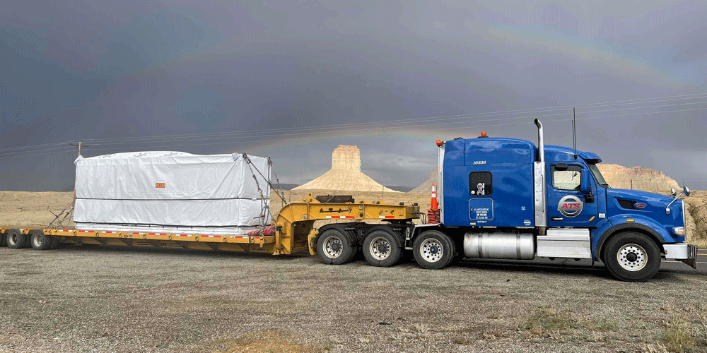 Parked semi with a tarped load. The sky in the background is cloudy but you can see rainbows.