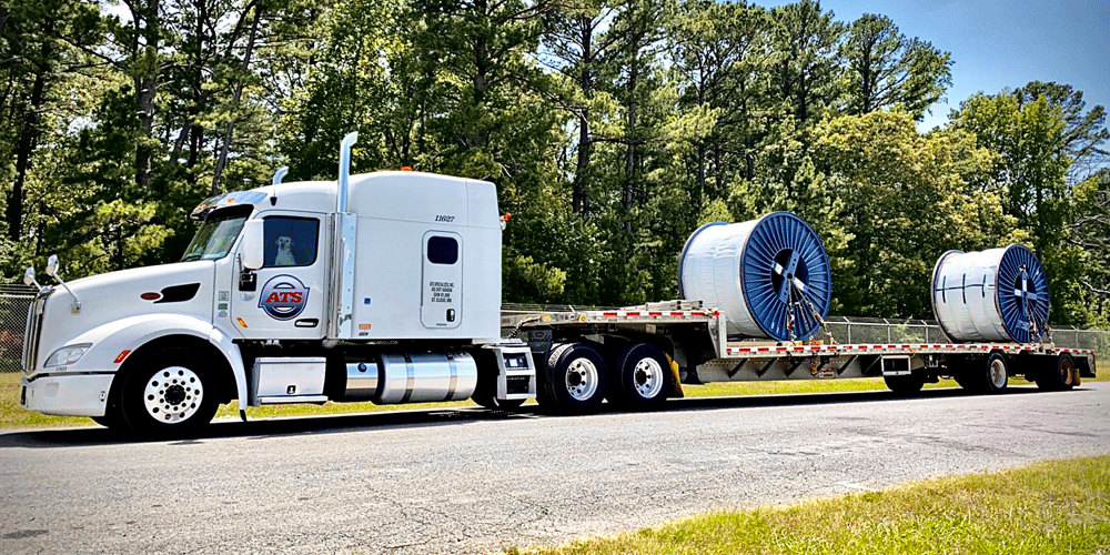 White semi hauling coils. A dog can be seen in the driver's seat.