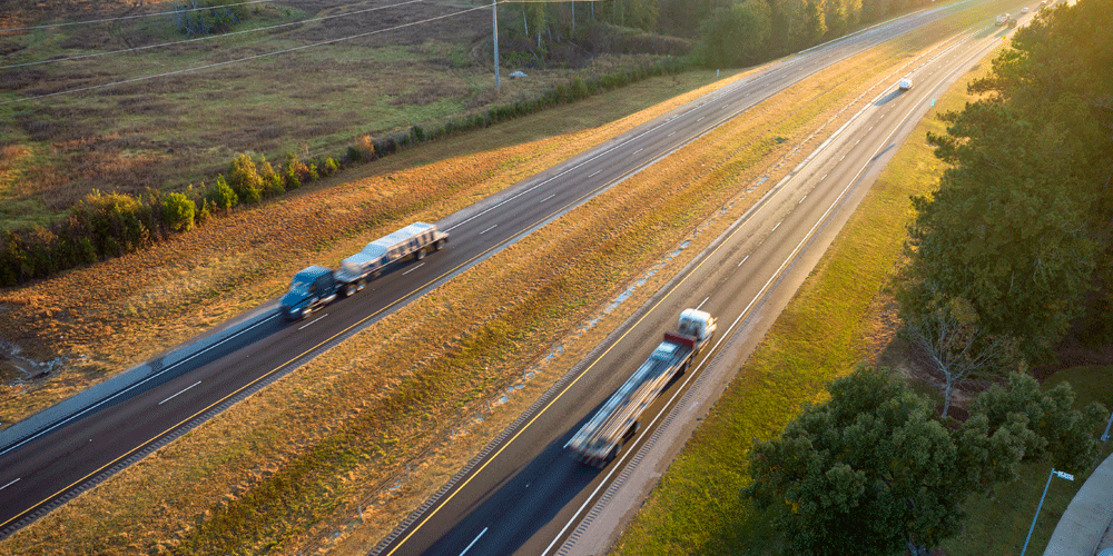 Bird's eye view of a wide open highway with two semis going in opposite directions.