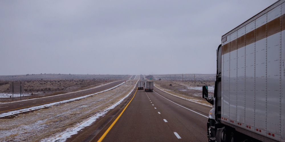 Three semi-trucks driving down a snowy desert road.