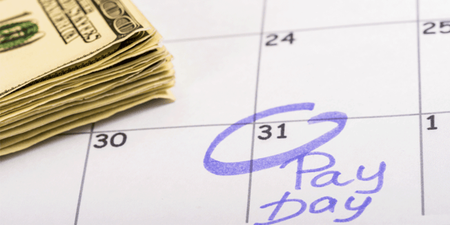 A stack of money sits atop a calendar with a pay day date circled in purple ink