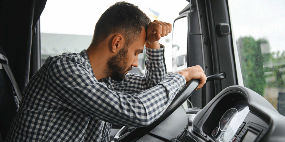 Tired and frustrated driver leaning over steering wheel.