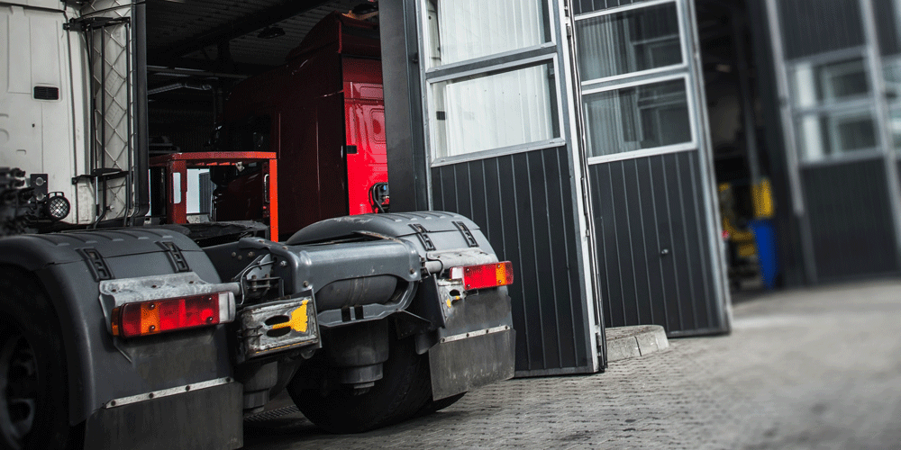 A semi-truck at the entrance to a shop. You can see multiple doors to let in other trucks.