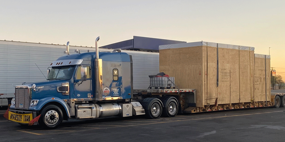 Two large oversized wooden boxes on a stepdeck flatbed trailer