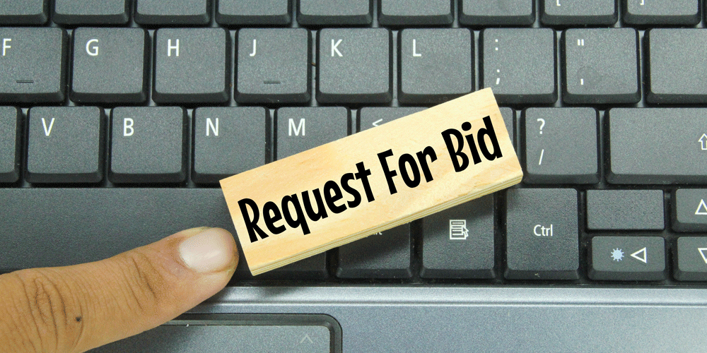 The words "request for bid" on a wooden block. It sits on a keyboard.
