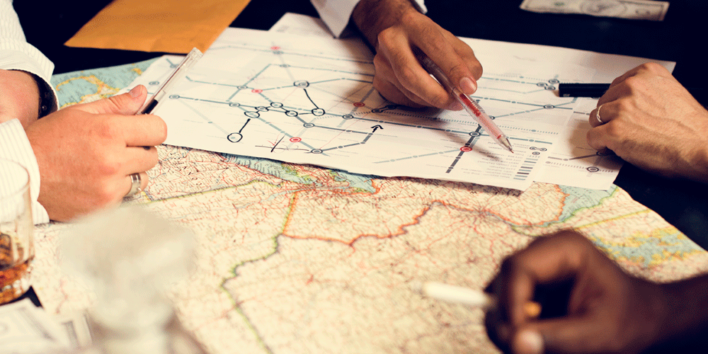 Planning loads by looking at a large map. Several hands point to spots on the map with pens.