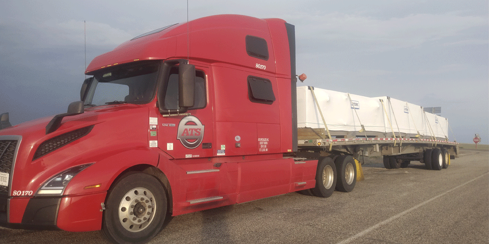 Red truck hauling white plastic covered load.