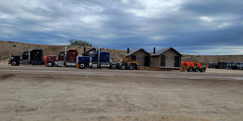 Three trucks lined up in a dirt field hauling park bathrooms.