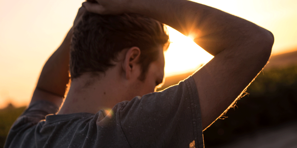 Man at sunset with his hands placed over his head. His back is to the camera.