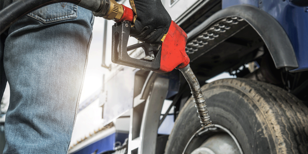 Close up view of gloved hand holding a fuel nozzle to fill up semi-truck.