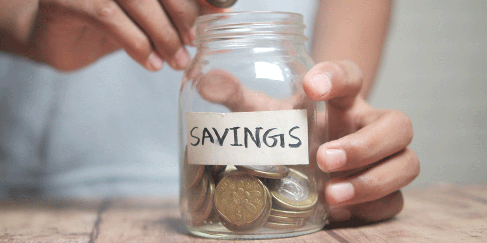 Zoomed in view of hands putting coins into a savings jar.