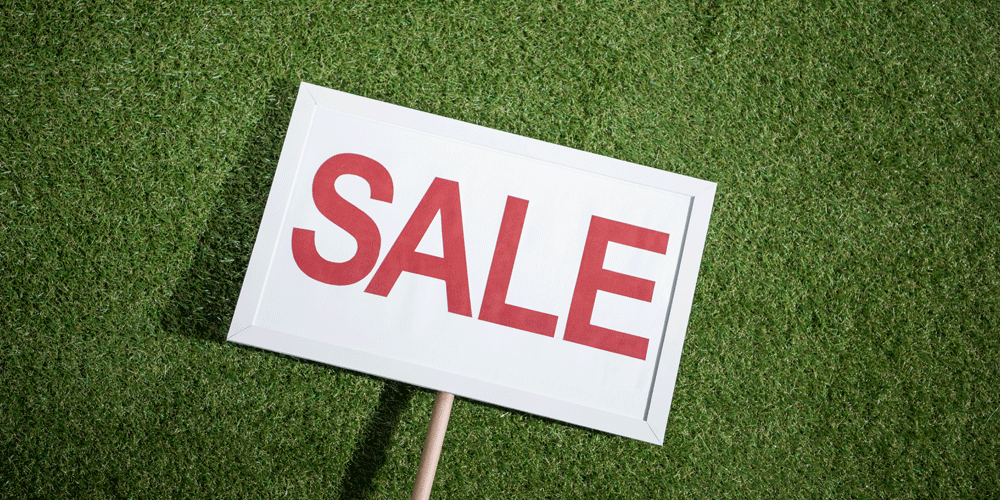 A white sign with the word "Sale" in red. It's laying on green grass.