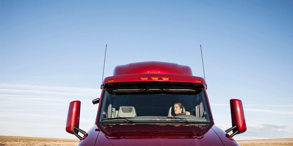 View into a semi-truck from in front of the windshield. A woman drives.