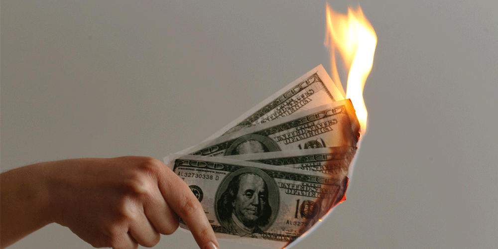 Hand holding 4 $100-dollar bills on fire.