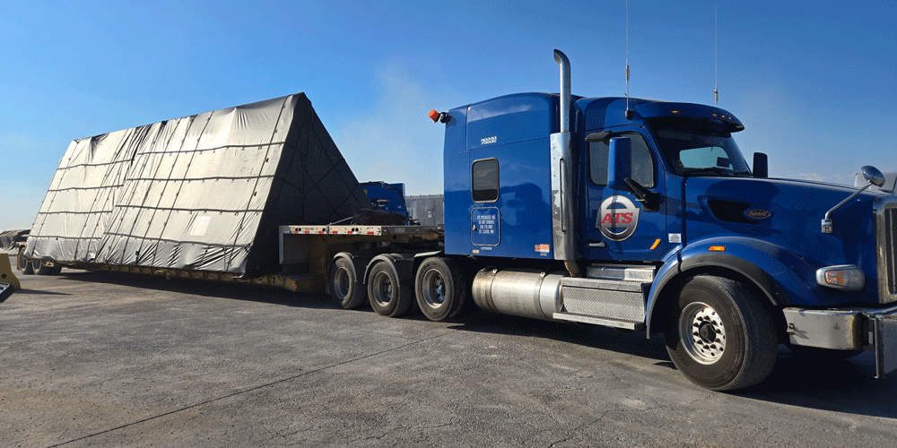 Triangular load on a step-deck trailer connected to a blue semi-truck.