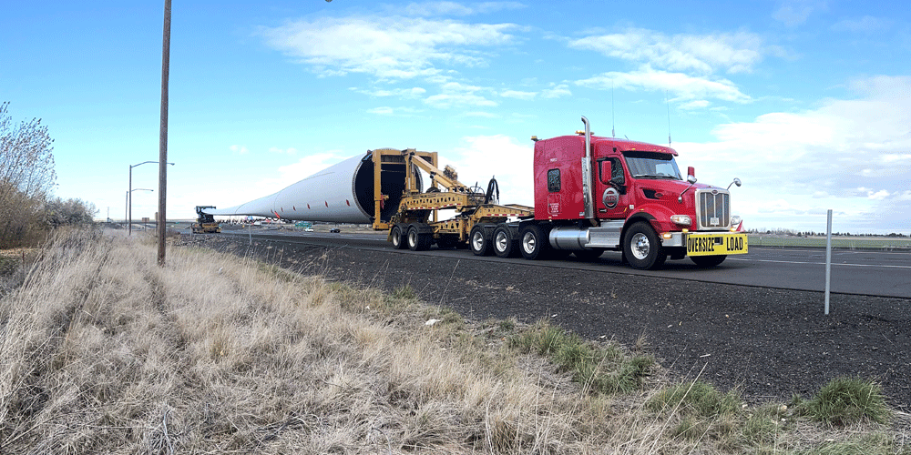 Wind blade trailer hauling a blade on the highway. The side of the highway is covered in dry grass.