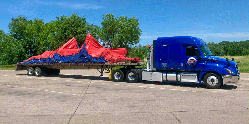 Blue semi-truck with a tarped flatbed load.