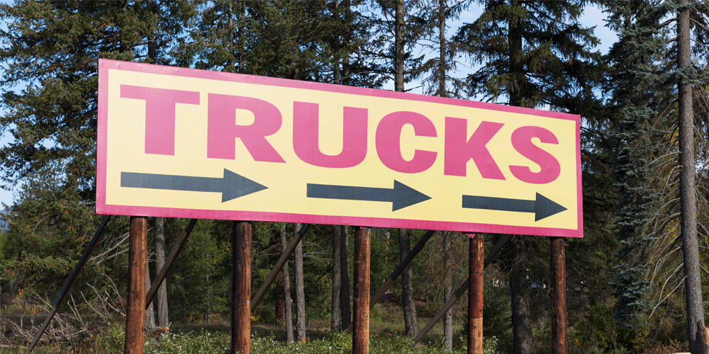 Large sign that says TRUCKS in red. There are three black arrows under the word trucks. The sign is yellow.