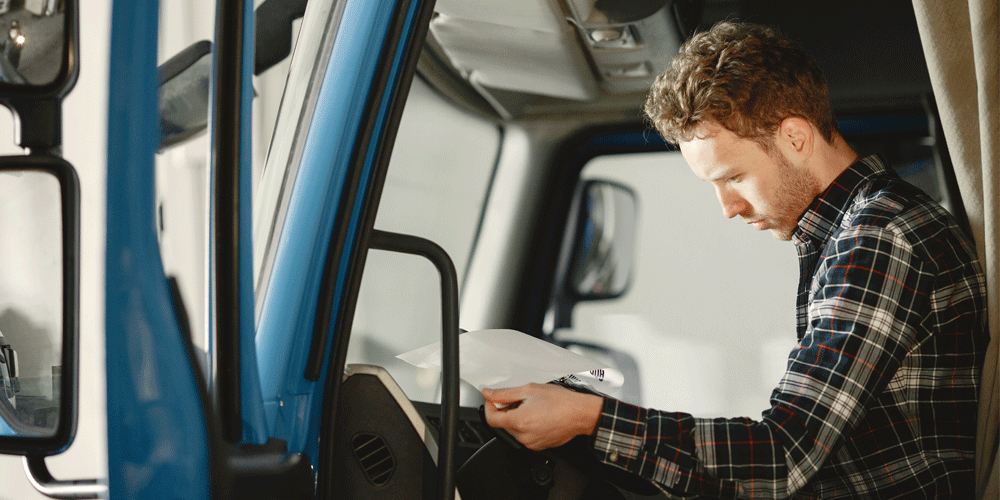 Truck driver in a plaid long sleeve shirt as he reviews paperwork. He sits in his semi.