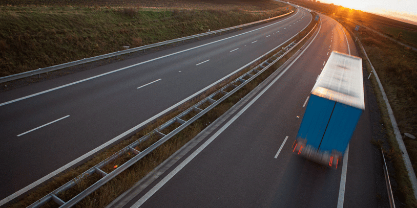 A dry van truck driving down an empty road