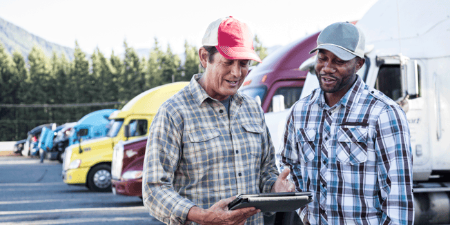 Driver manager and driver talking in truck parking lot as a row of semi-trucks sit parked