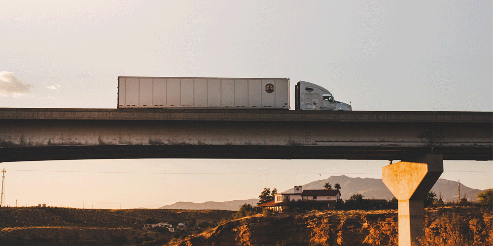 Semi-truck with dry van trailer driving over bridge.