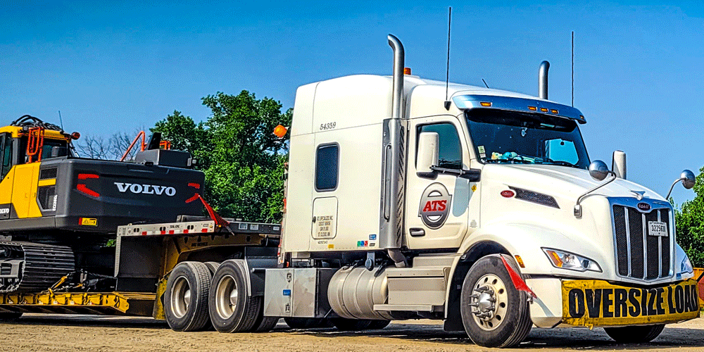 White semi-truck hauling Volvo construction equipment.