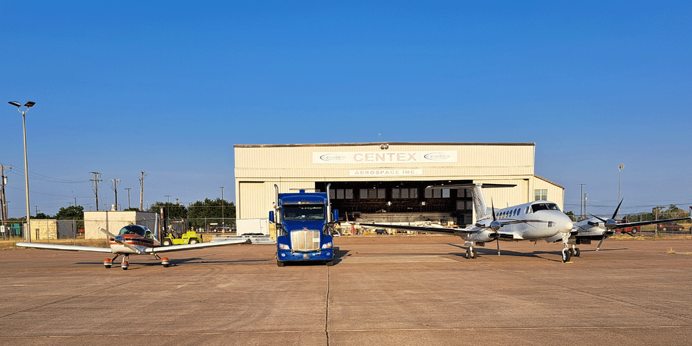A blue truck in-between two small private planes at an airplane hangar.