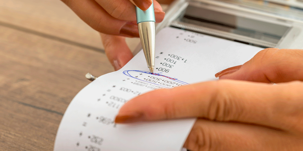 A woman with painted fingernails circling a number on a receipt.