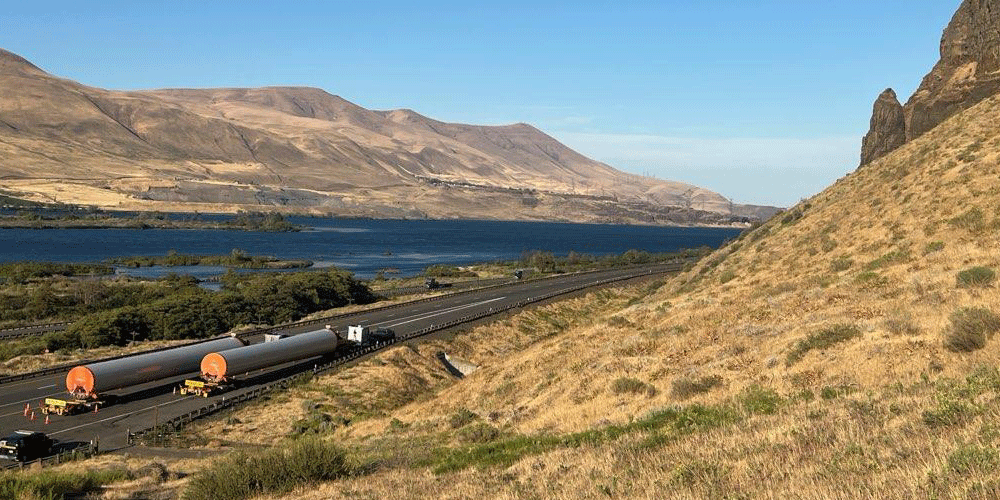 Two tanker trucks driving on a beautiful mountain road.