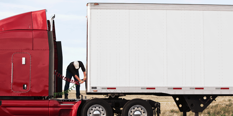 Truck driver connecting power cables between semi-truck and trailer.