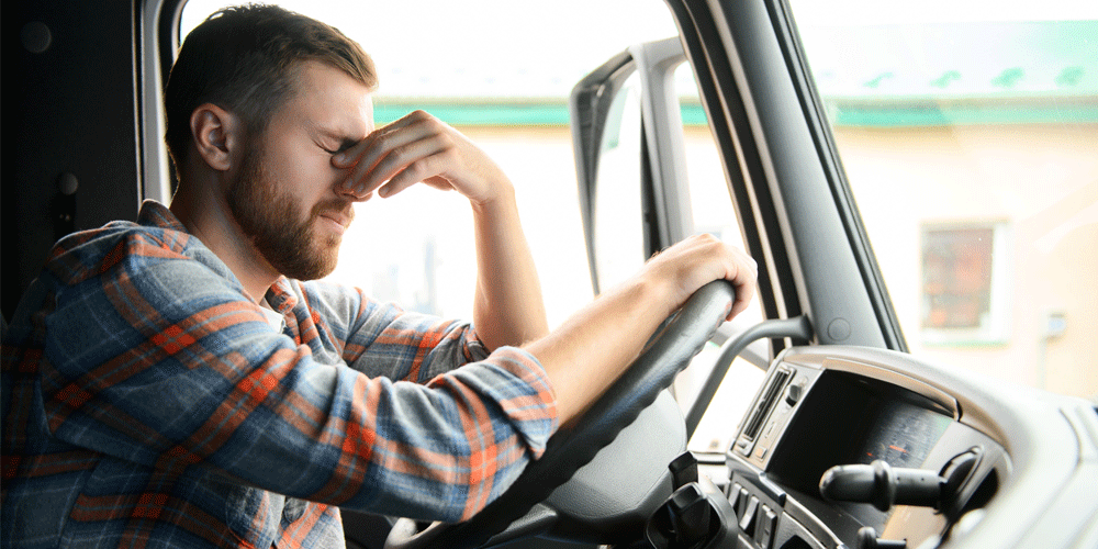 Frustrated, tired driver holding the bridge of his nose as he sits behind the wheel of his truck.