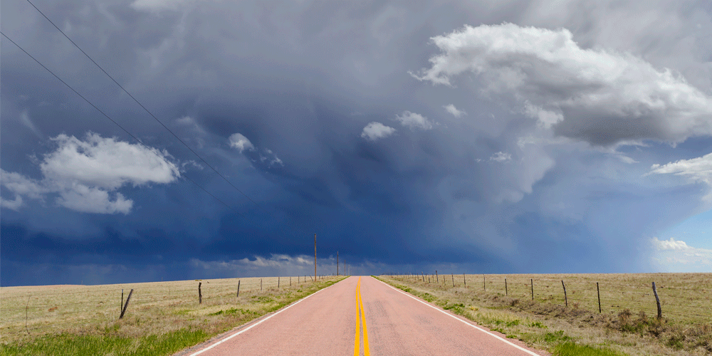 An open road in the Colorado country with storm clouds in the sky.