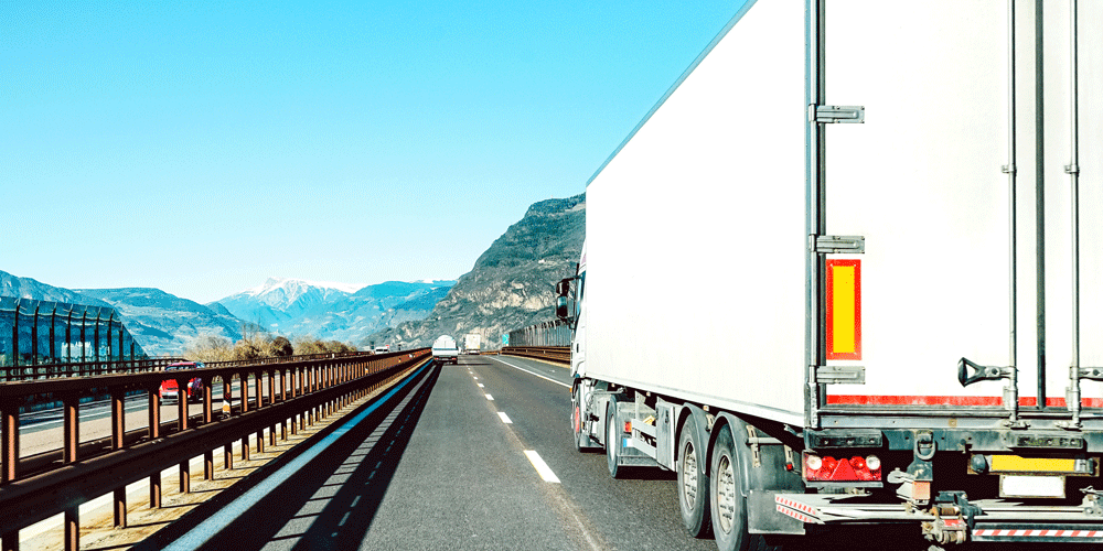 Backside view of a dry van trailer going down the road with mountains in the background