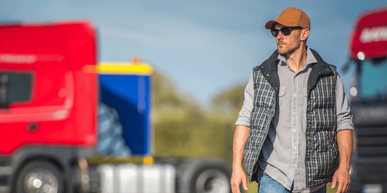 Truck driver outside in parking lot with trucks in background