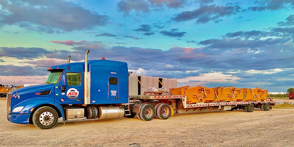 Blue ATS truck hauling construction parts. It's dusk and the sky has a few clouds.