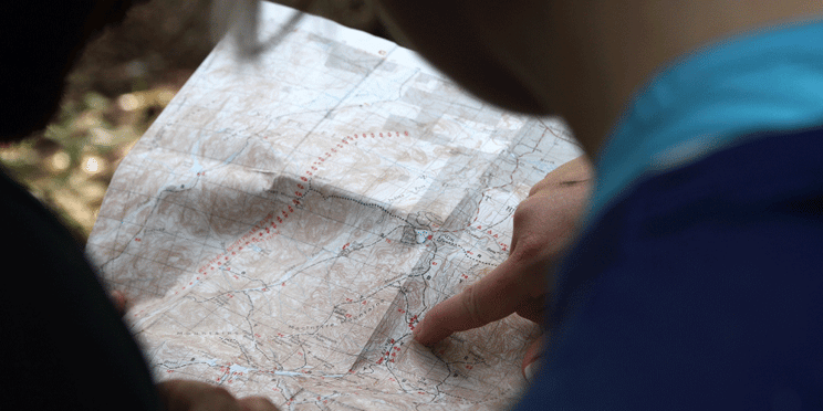 Two individuals holding out a road map. One person points at a spot on the map.