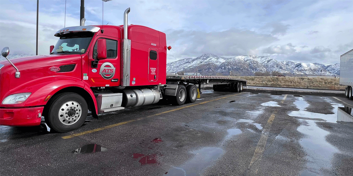 ATS semi-truck with flatbed trailer in parking lot with mountains in background; truck abandonment guide for truck drivers; Anderson Trucking Service