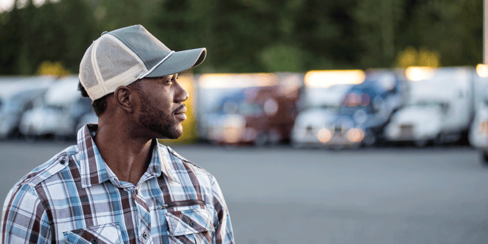 Truck driver stands pensively in parking lot, looking off into the distance