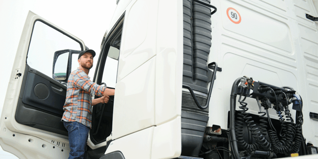 Driver in ball cap stepping out of white semi-truck. Why DOD drivers earn more