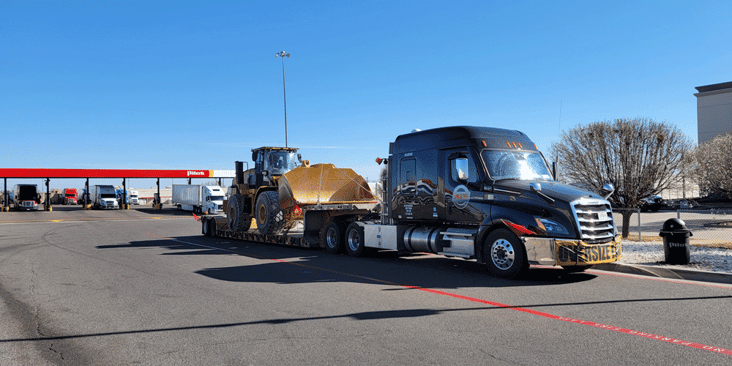 Black ATS truck with flatbed load parked in front of a Pilot truck stop.