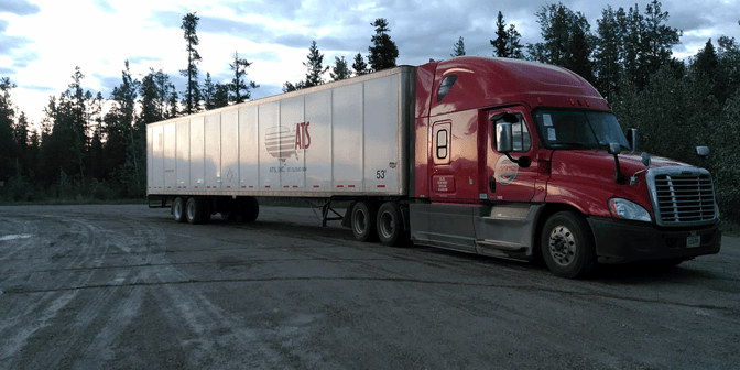 Red ATS truck and van trailer parked in front of a group of trees.