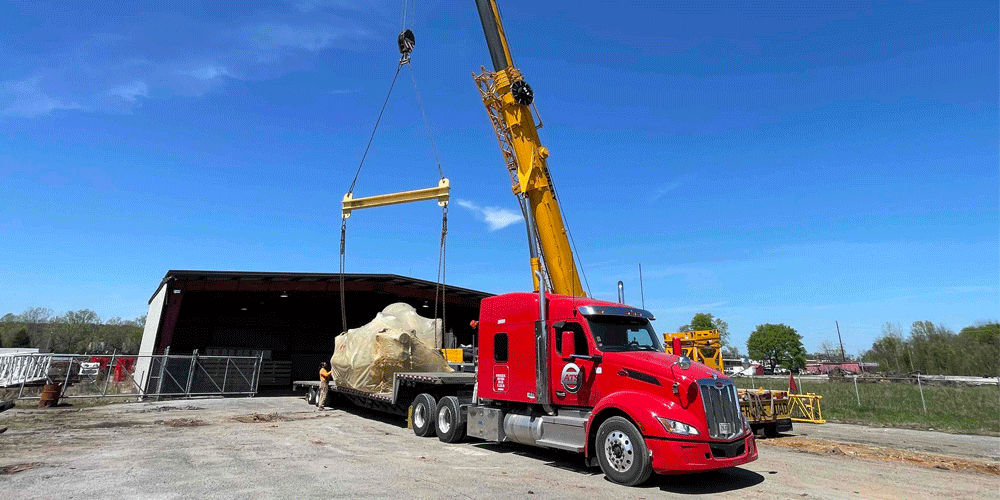 Crane loading oversized tarped freight onto ATS truck and flatbed trailer.
