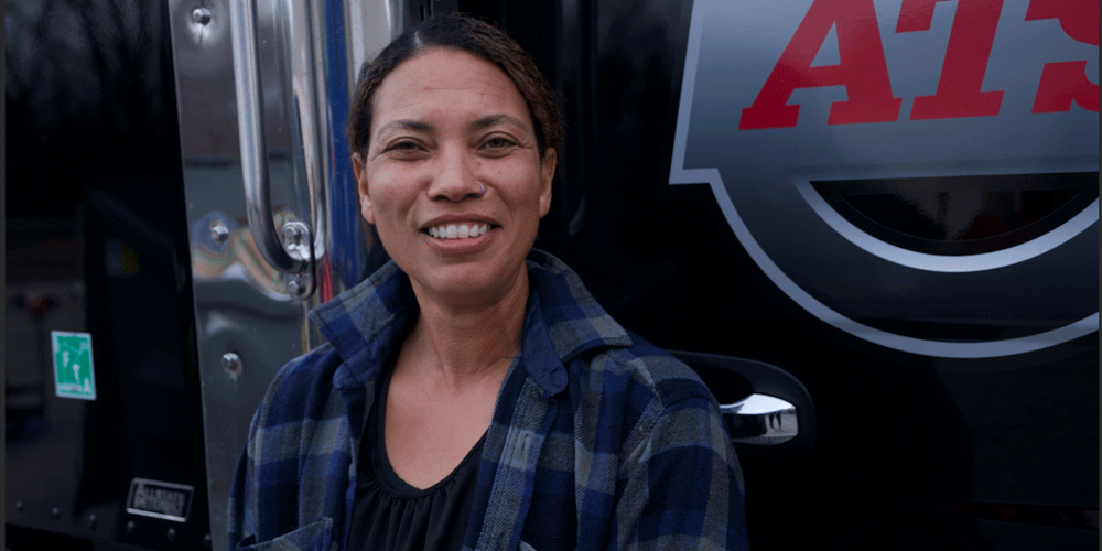 Smiling female truck driver in front of her semi-truck.