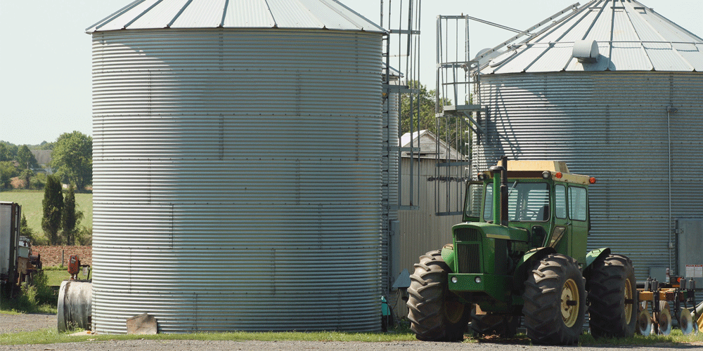 Green farm tractor in front of two silos.
