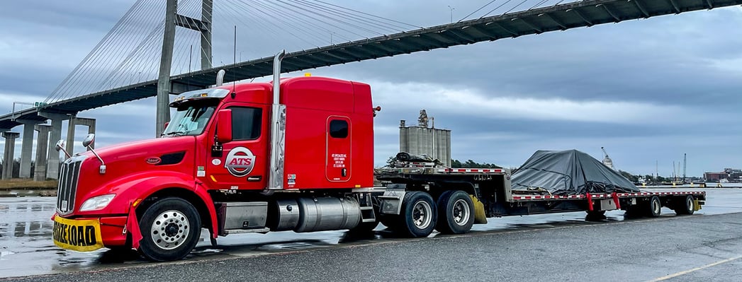 An ATS truck hauling a step-deck flatbed with a tarped load