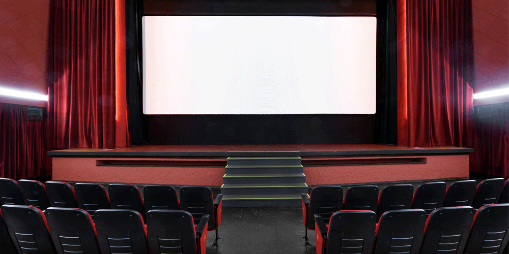 Empty movie theater with black seats, a blank screen, and red curtains.