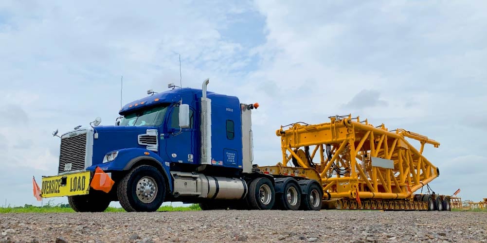 Blue Freightliner heavy haul truck with large equipment on trailer