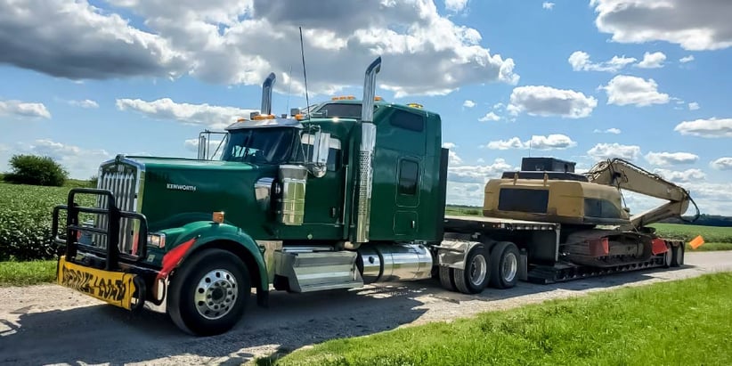 Green Semi-truck with large construction equipment on trailer